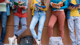 Junge Menschen stehen an einer Wand gelehnt und halten Büchern in den Händen