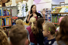 Eine Frau in einem Raum mit Bücherregalen erklärt einer Gruppe Kinder etwas